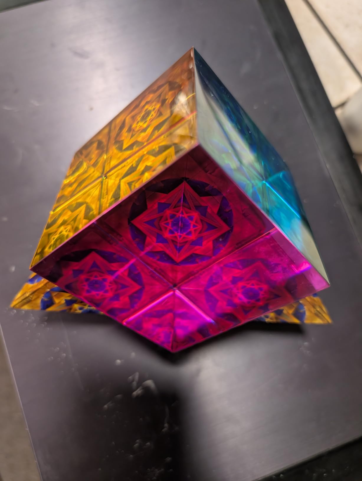 Customer photo of a Shashibo folded to a point on a dark desk, showing magenta, gold and teal star patterns on its faces