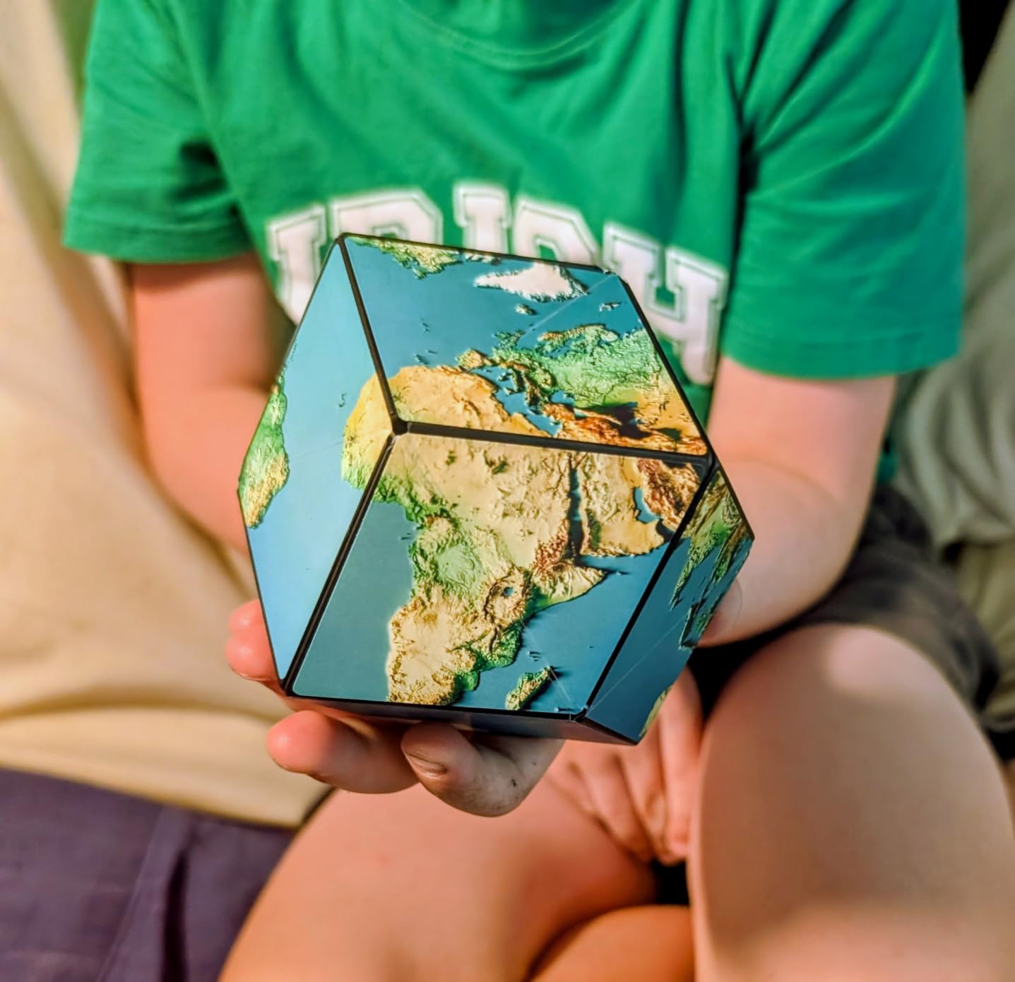 Customer photo of a child in a green shirt holding a Shashibo Earth cube showing Africa and Europe in satellite relief