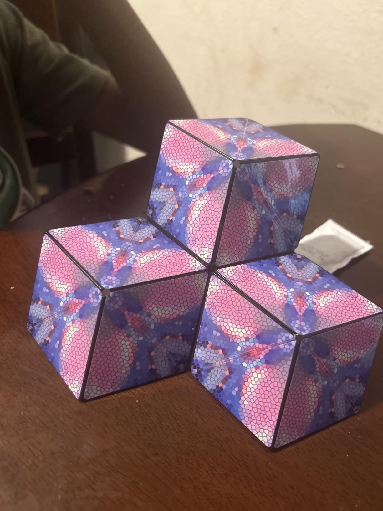 Customer photo of three pink and violet mosaic-pattern Shashibo cubes joined together on a dark wood table