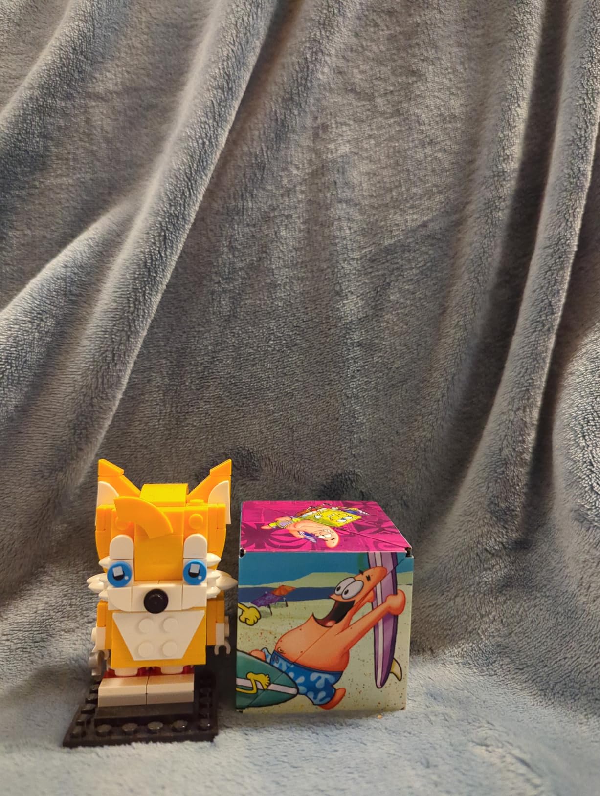 Customer photo of a closed SpongeBob Shashibo cube next to a small Lego figure, showing how little space it takes